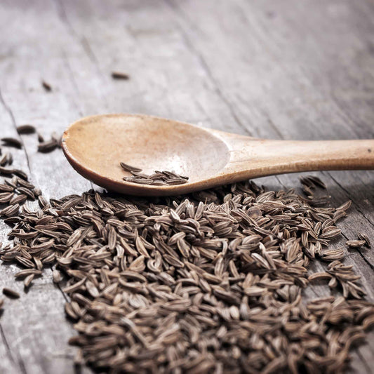 A close-up of light brown cumin seeds scattered on a dark background.