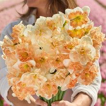 A person holding a bouquet of butterfly blend daffodil bundle in a garden setting.