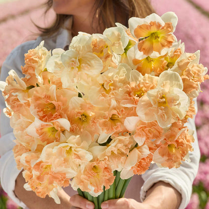 A person holding a bouquet of butterfly blend daffodil bundle in a garden setting.