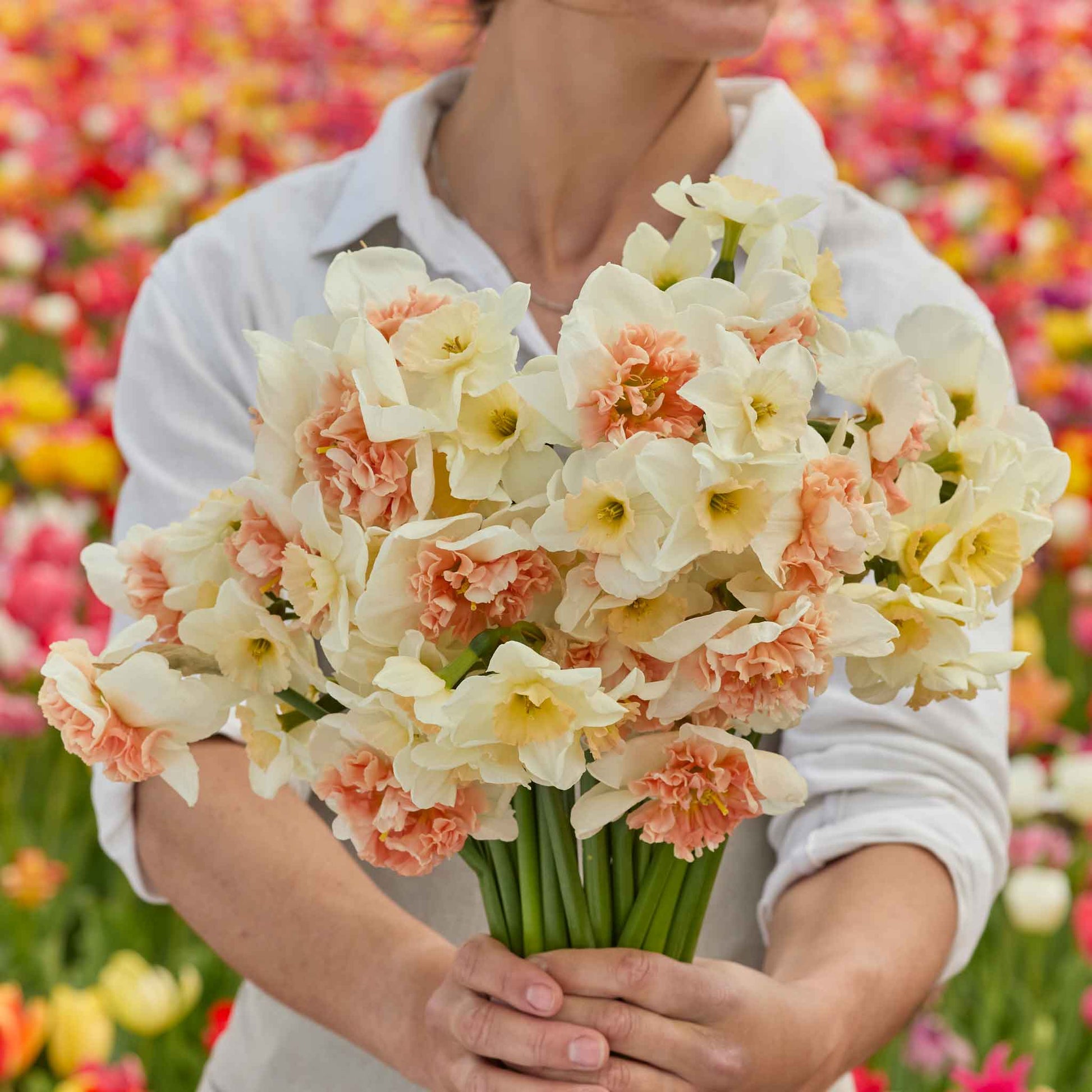 A person holding a bouquet of Double Take Mix daffodil flowers in a garden setting.