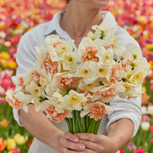A person holding a bouquet of Double Take Mix daffodil flowers in a garden setting.