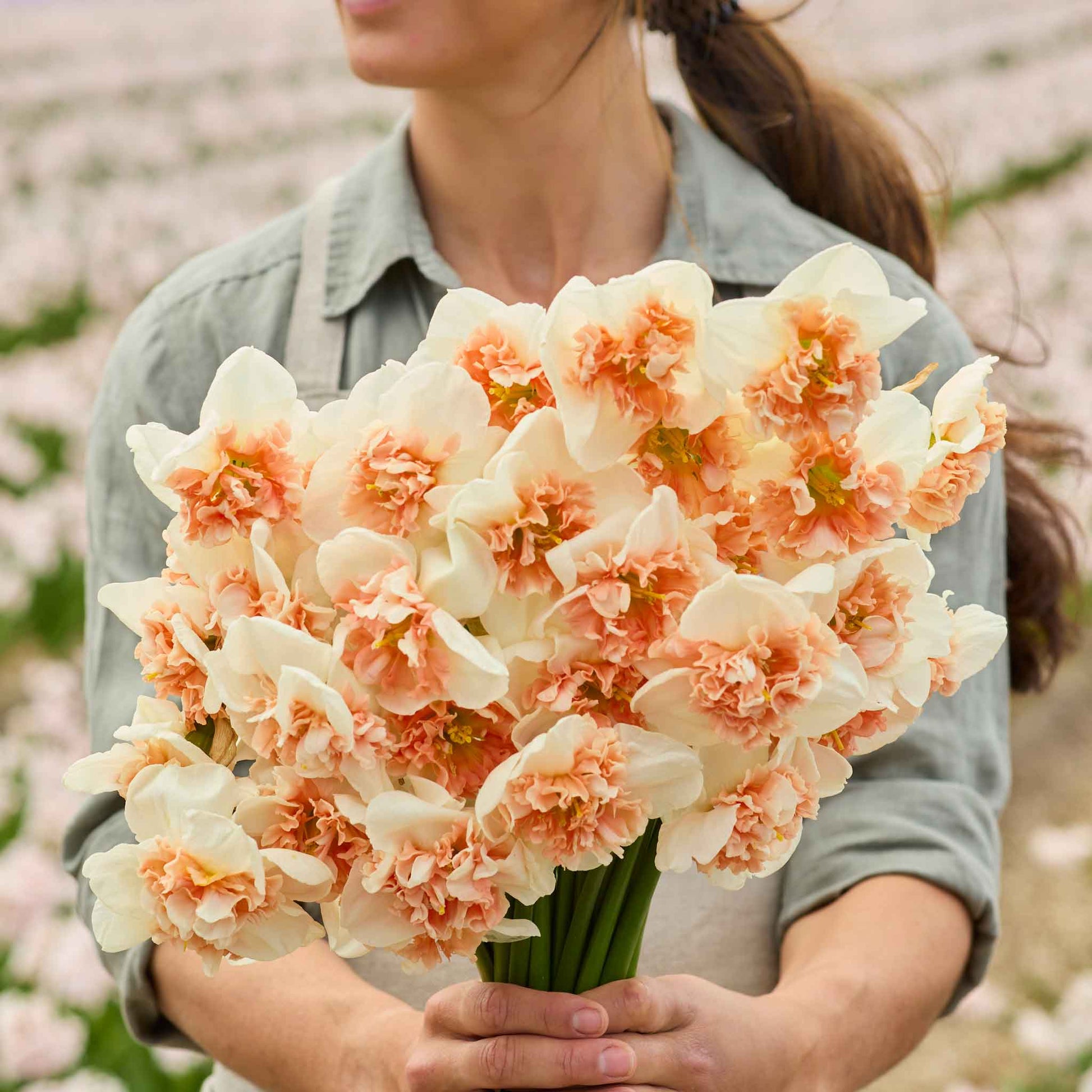 A person holding a bouquet of Fire Drill daffodil flowers in a garden setting.