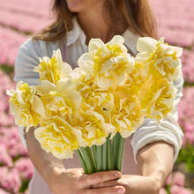 A person holding a bouquet of Lingerie daffodil flowers in a garden setting.