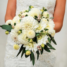 Person in a white dress holding White mix dahlias in a bouquet in a neutral setting.