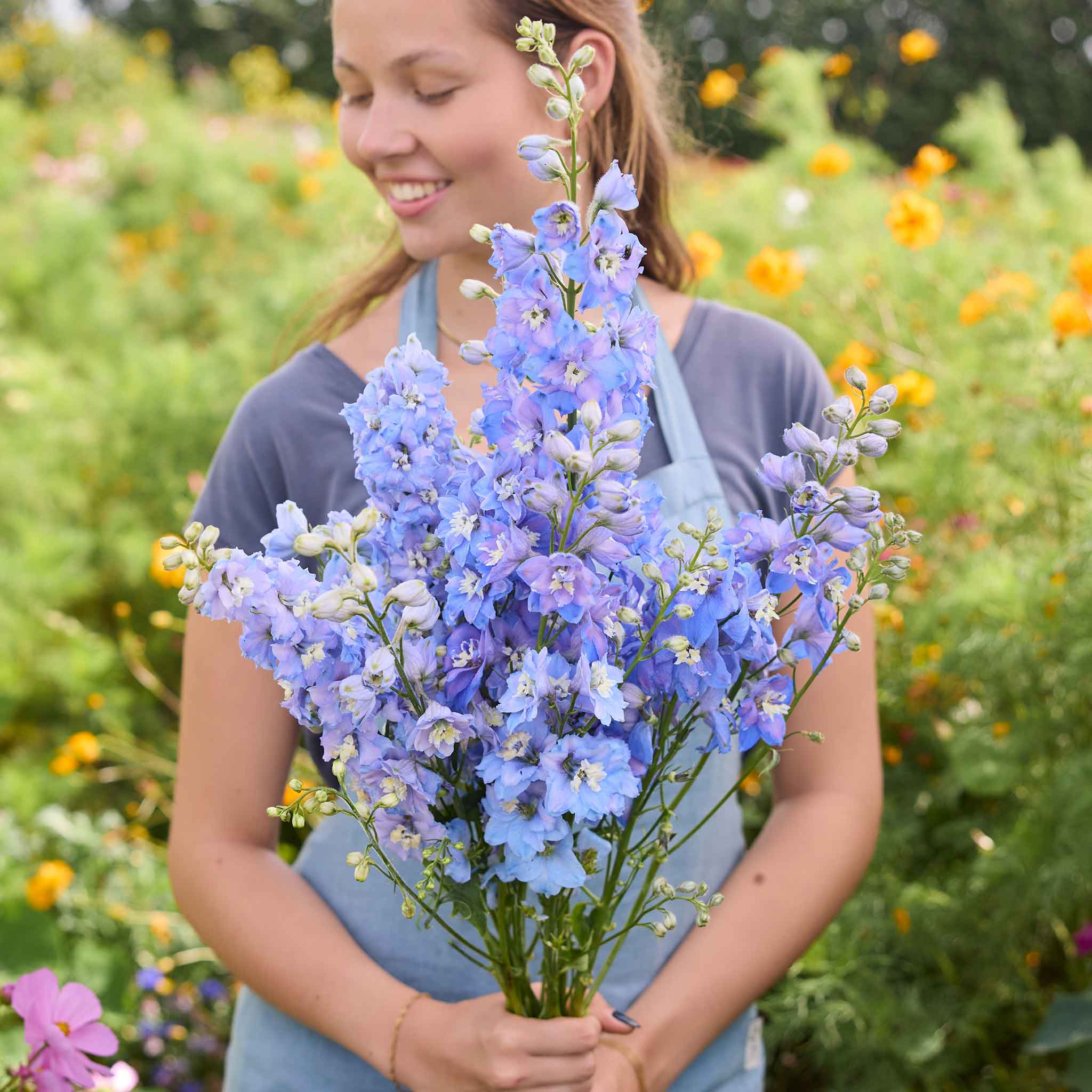 Woman holding a bouquet of sky blue white bee delphina flowers in a garden setting