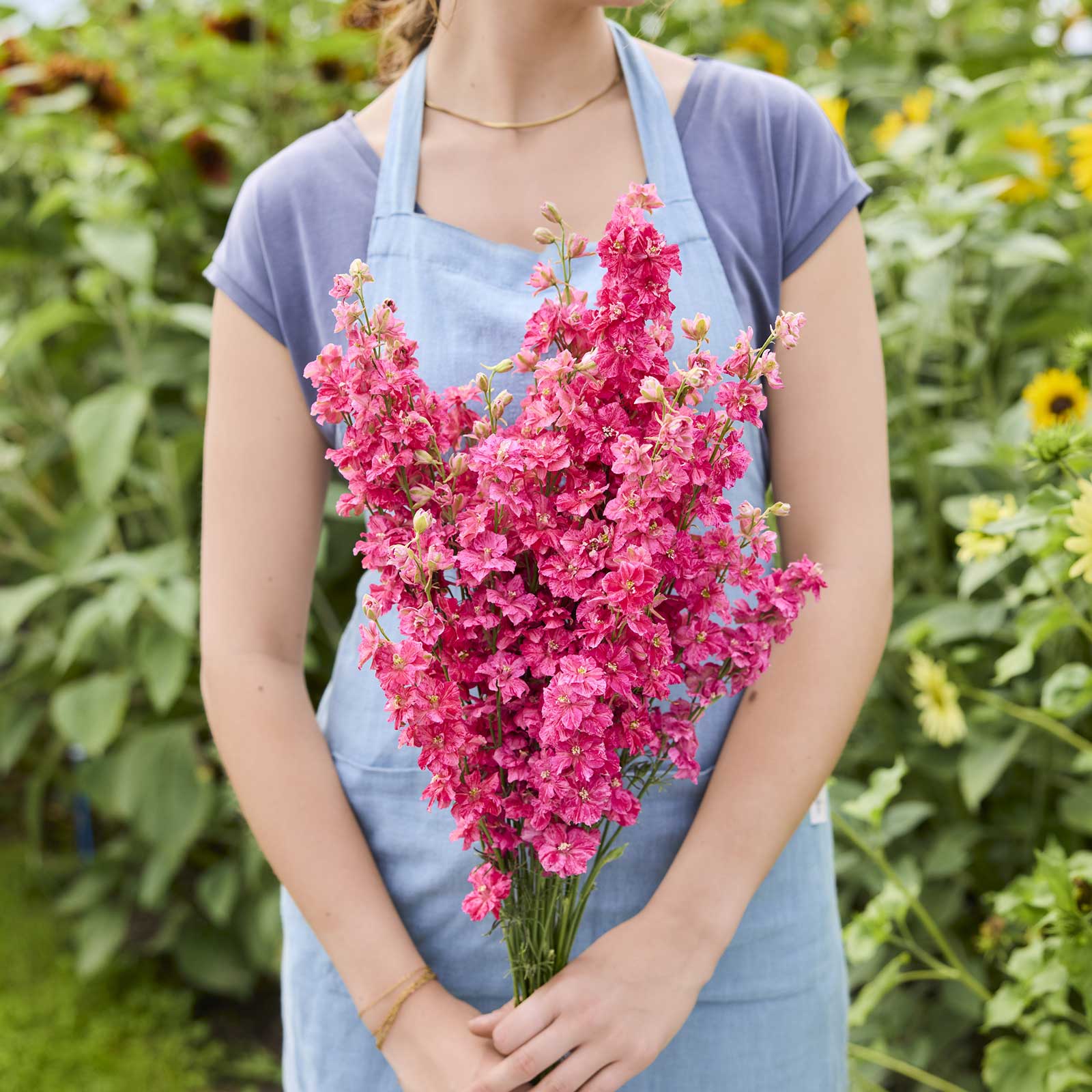 A person holding a bouquet of larkspur king size scarlet flowers in a garden setting.