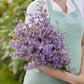 Person holding a bouquet of misty lavender larkspur flowers with a blurred green background