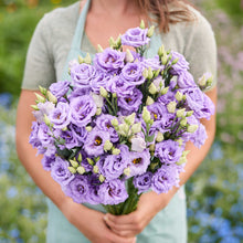 A person holding a bouquet of lisianthus corelli lavender flowers in a garden setting.