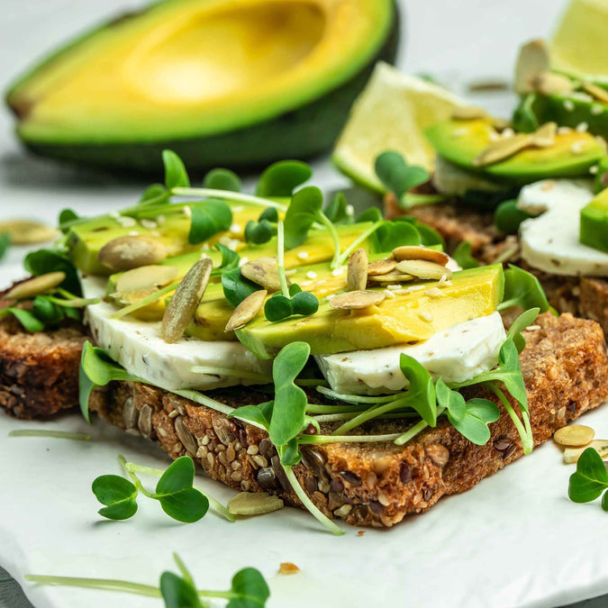 Avocado toast with microgreen sprouts and seeds on a white plate