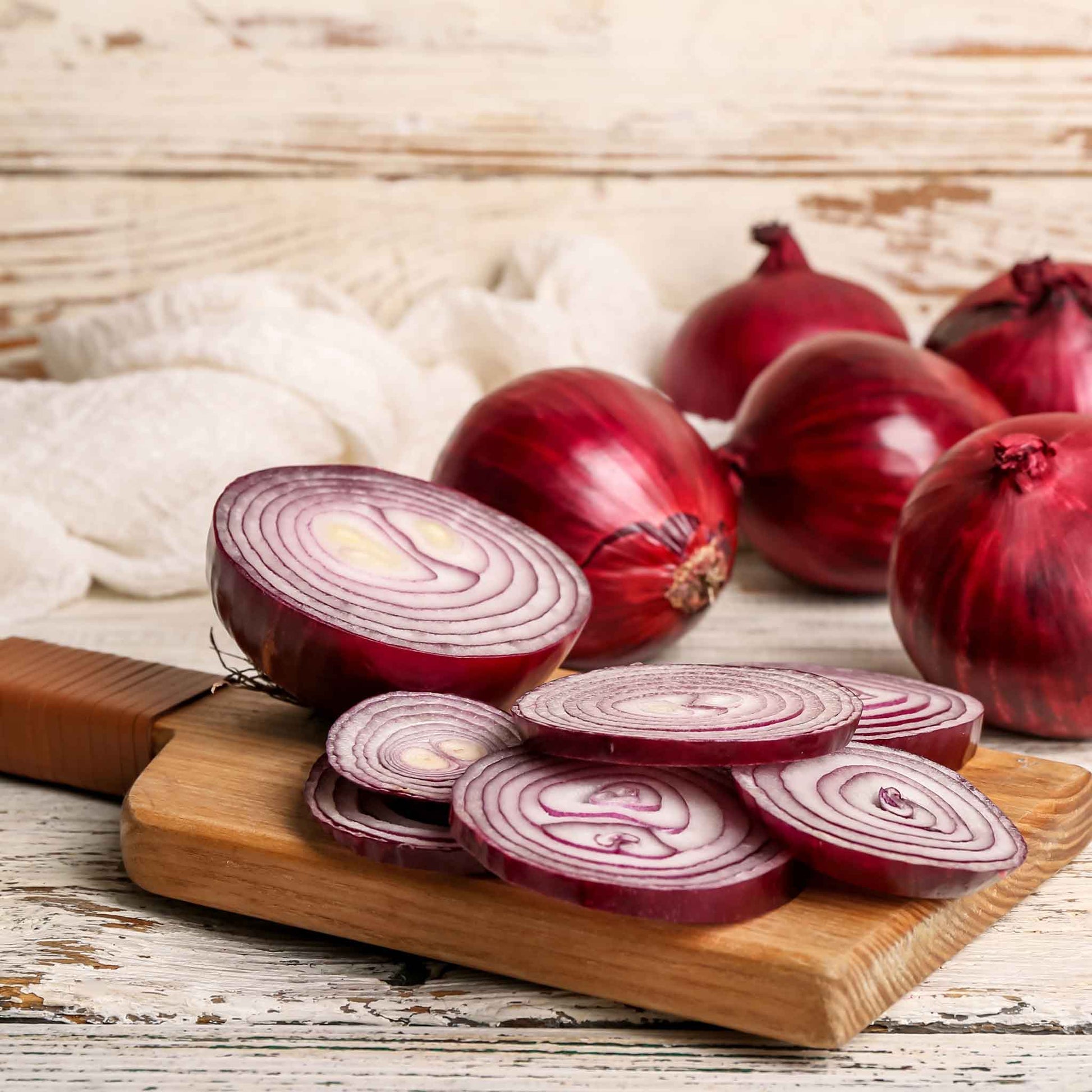 Vibrant Red Grano onions on a wooden background with several sliced onions in the foreground.