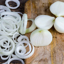 A close-up of several sliced Ringmaster White Sweet Spanish onions with thin, papery skins, resting on a rustic wooden surface.