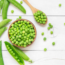 A bowl and spoon full of Wando peas on a white surface.