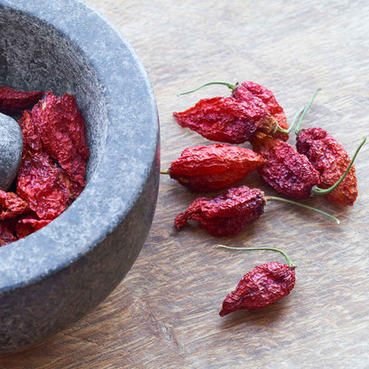 Several shriveled, bumpy, red Bhut Jolokia 'Ghost' peppers laid out next to a bowl ready for use.