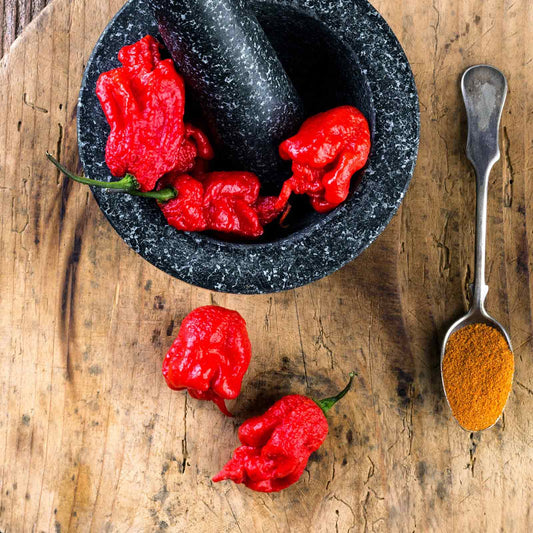 A vivid red Carolina Reaper pepper, known for its extreme heat, is shown close-up.