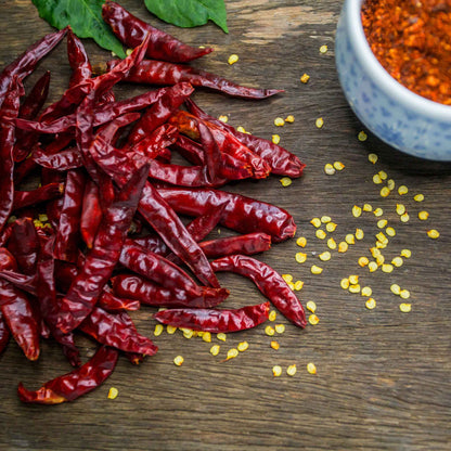 Dried red chile de arbol peppers, with a focus on their elongated, slender shape and deep red color.