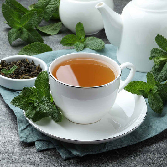 White cup of Peppermint tea with mint leaves on a gray surface
