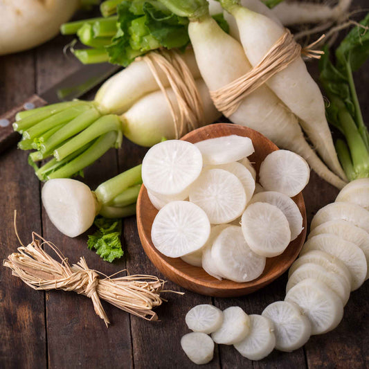 Several large, white Japanese Minowase Daikon radishes are shown, some with leafy green tops.