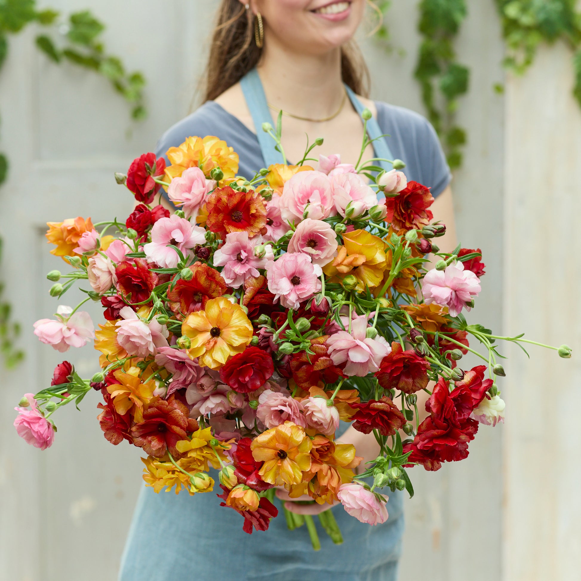 Vibrant ranunculus bright mix bouquet held by a person on a light blue backdrop