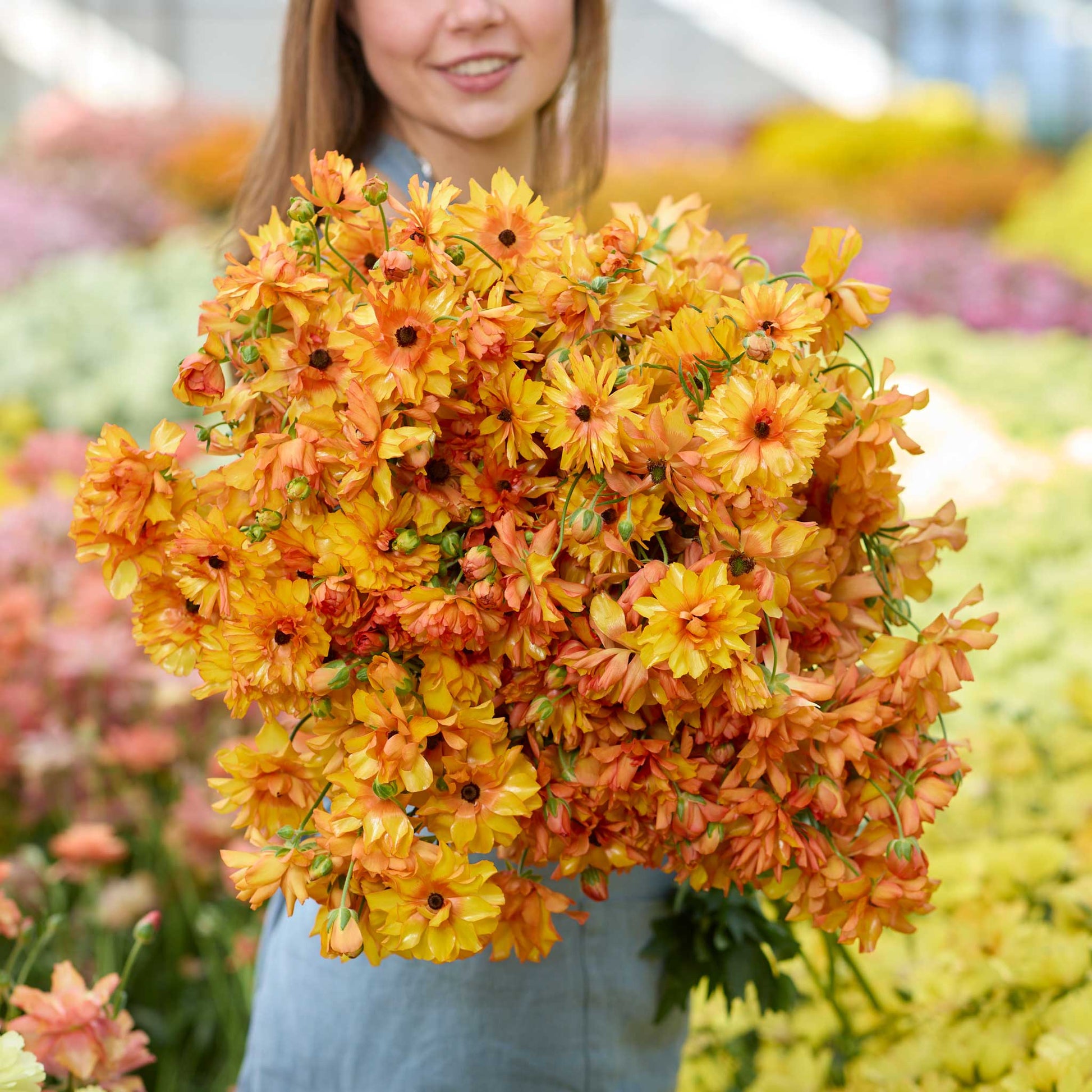 Person holding a large bouquet of orange and yellow butterfly phosphorus ranunculus flowers in a garden setting