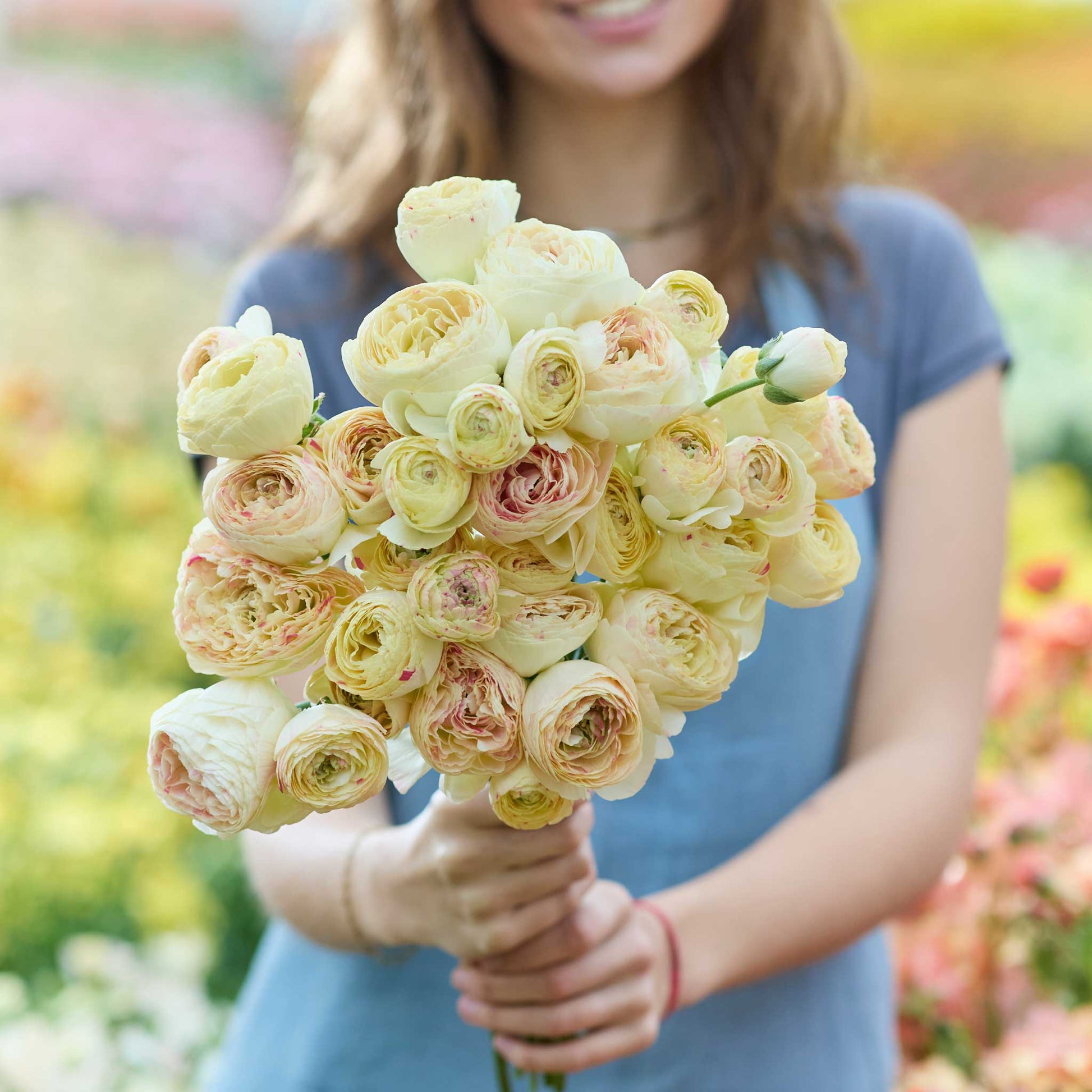 Person holding a bouquet of yellow romance hydra ranunculus flowers with a garden background