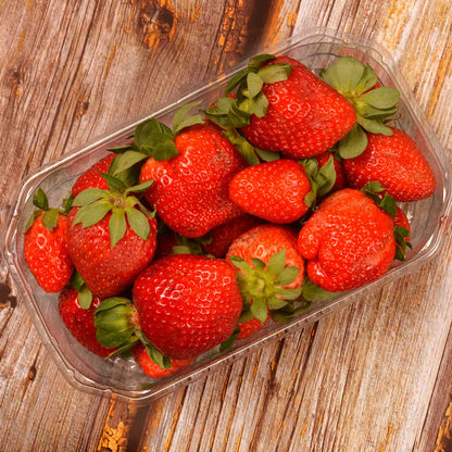 Freshly harvested red Eclair strawberries in a plastic container on a wooden surface