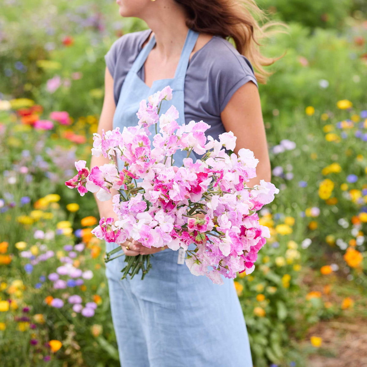 A person holding a bouquet of pink promse sweet pea flowers in a natural setting