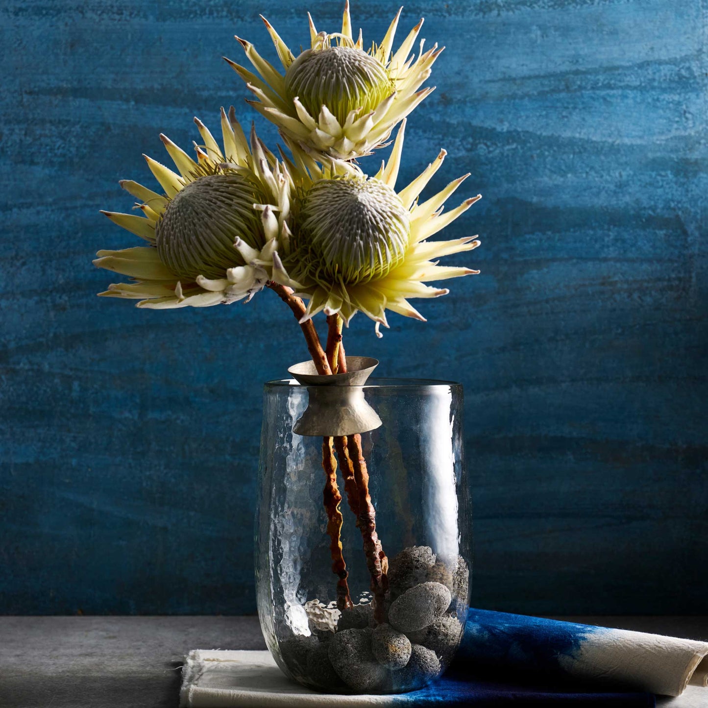 The collective floral bouquet ring shown holding the bare stems of three flowers in a clear vase with rocks at the bottom.