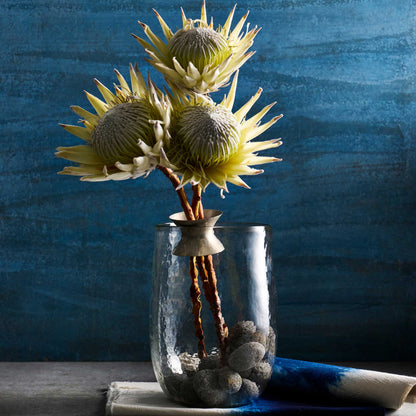 The collective floral bouquet ring shown holding the bare stems of three flowers in a clear vase with rocks at the bottom.