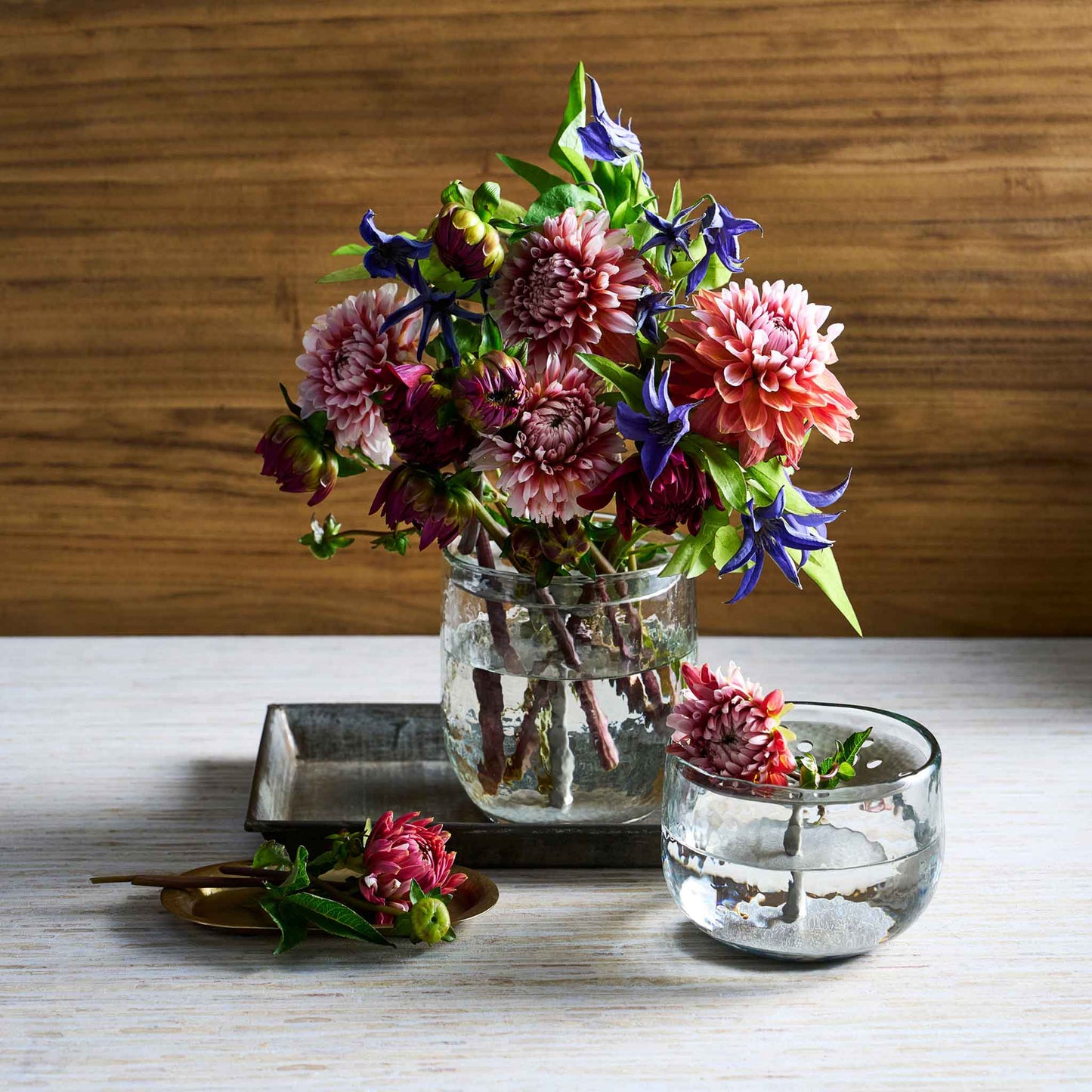 A floral bouquet using the collective pebbled vase and flower frog on a white table and wooden background