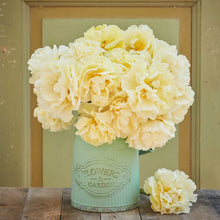 Light yellow avant garde tulips in a green vase labeled 'Flowers & Garden' on a wooden surface with a green background.