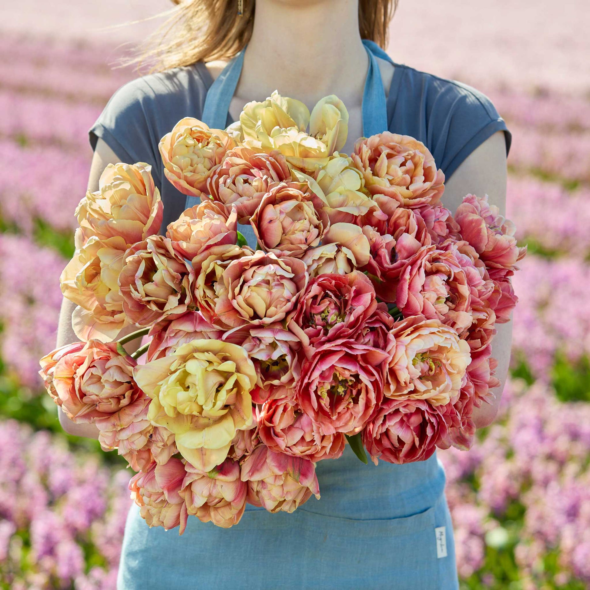 A person holding a pink and yellow bouquet from the la belle epoque and copper image tulip bundle