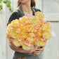 Person holding a large bouquet of yellow and pink creme upstar tulips in a greenhouse setting
