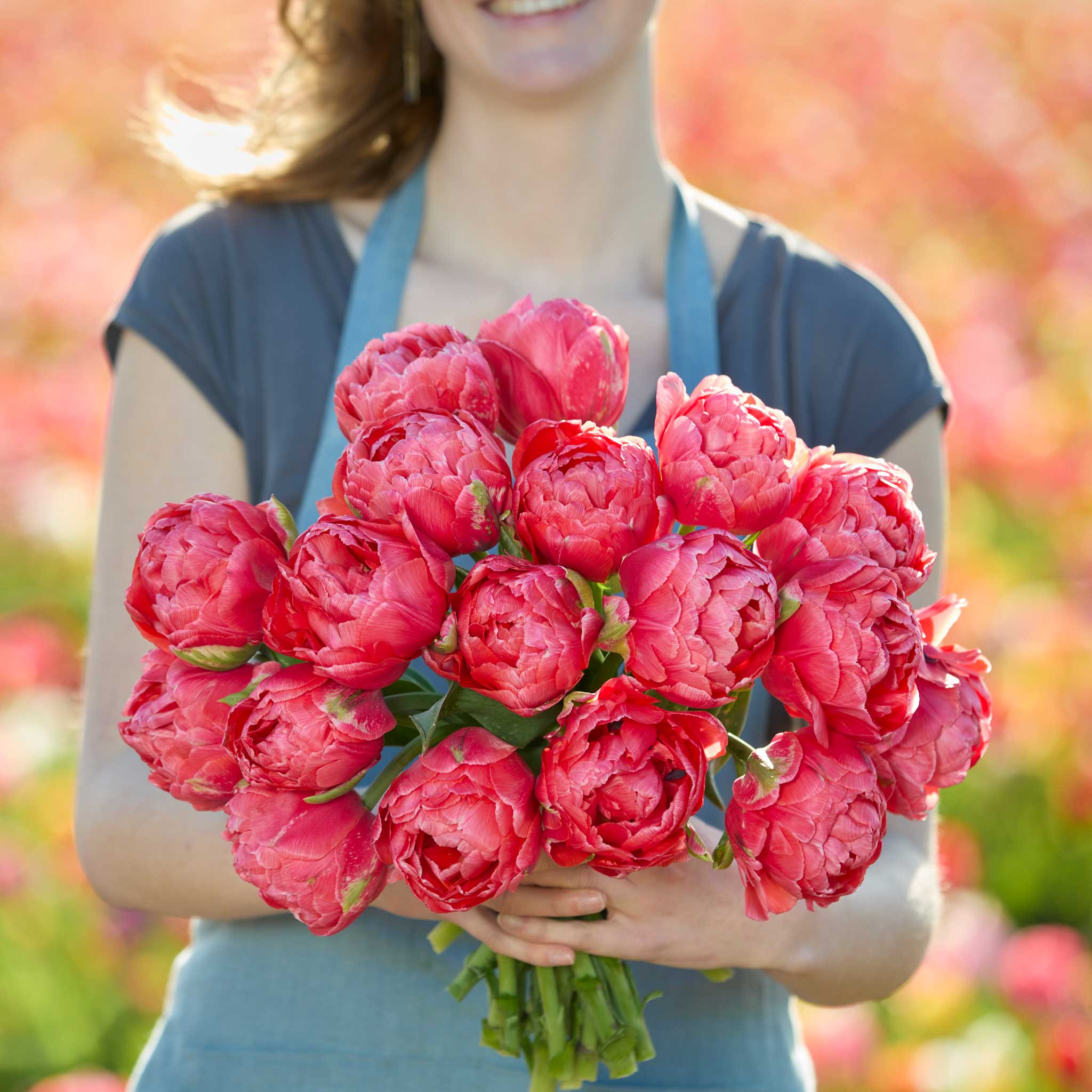 Person holding a bouquet of red etched salmon tulips with a blurred floral background