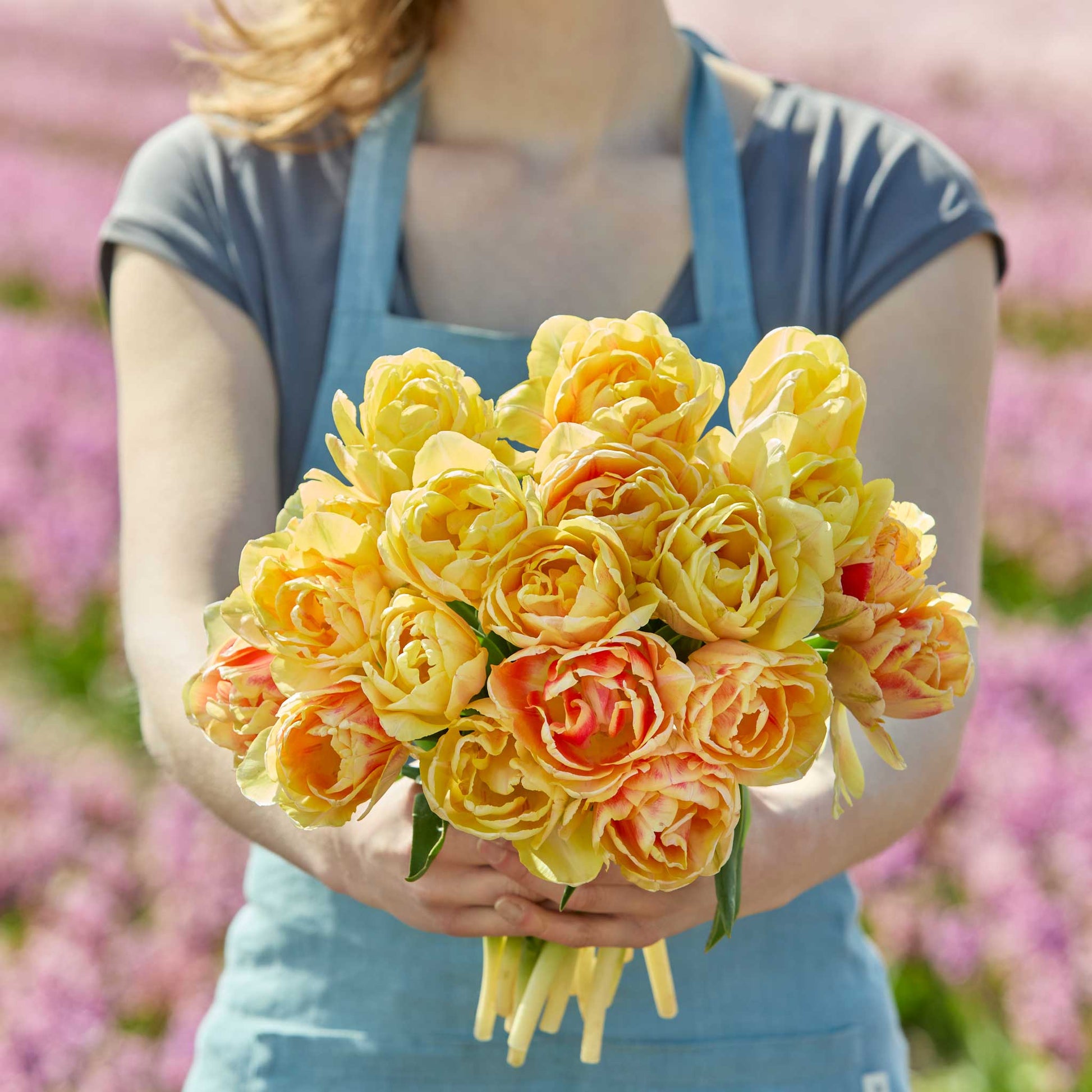 Person holding a bouquet of yellow and orange foxy foxtrot tulips with a blurred floral background