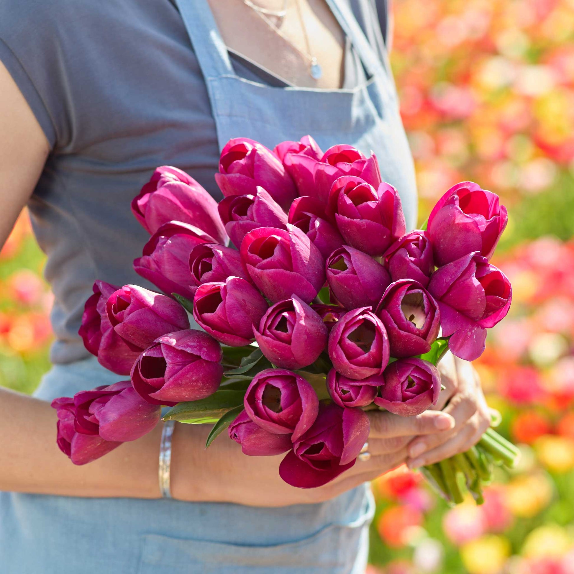 Person holding a bouquet of pink roeska tulips with a blurred floral background