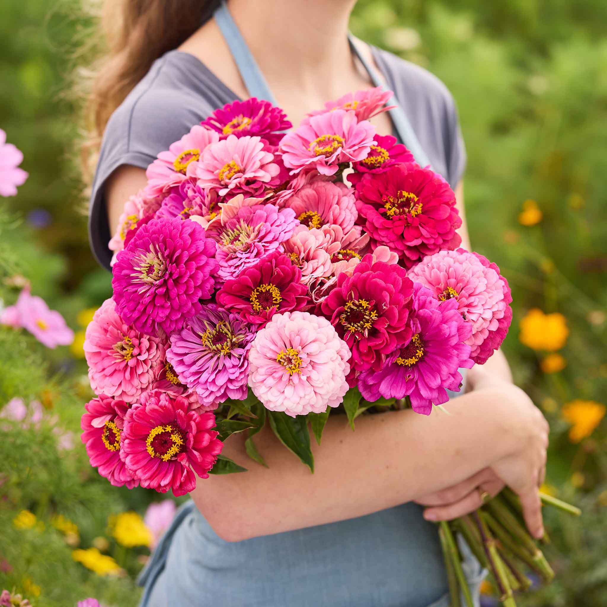 Person holding a bouquet of art deco mix zinnia flowers in a garden setting
