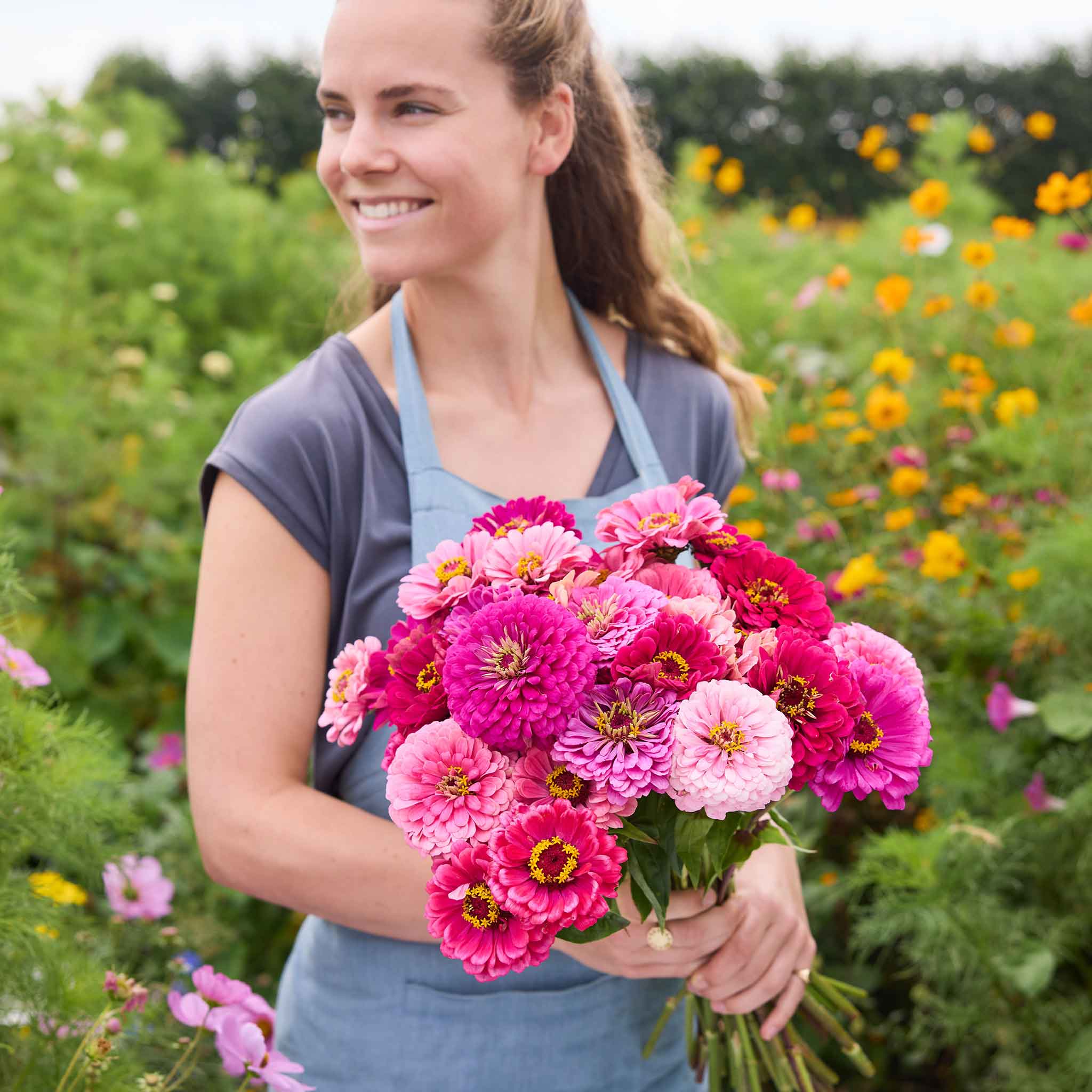 Person holding a bouquet of art deco mix zinnia flowers in a garden setting