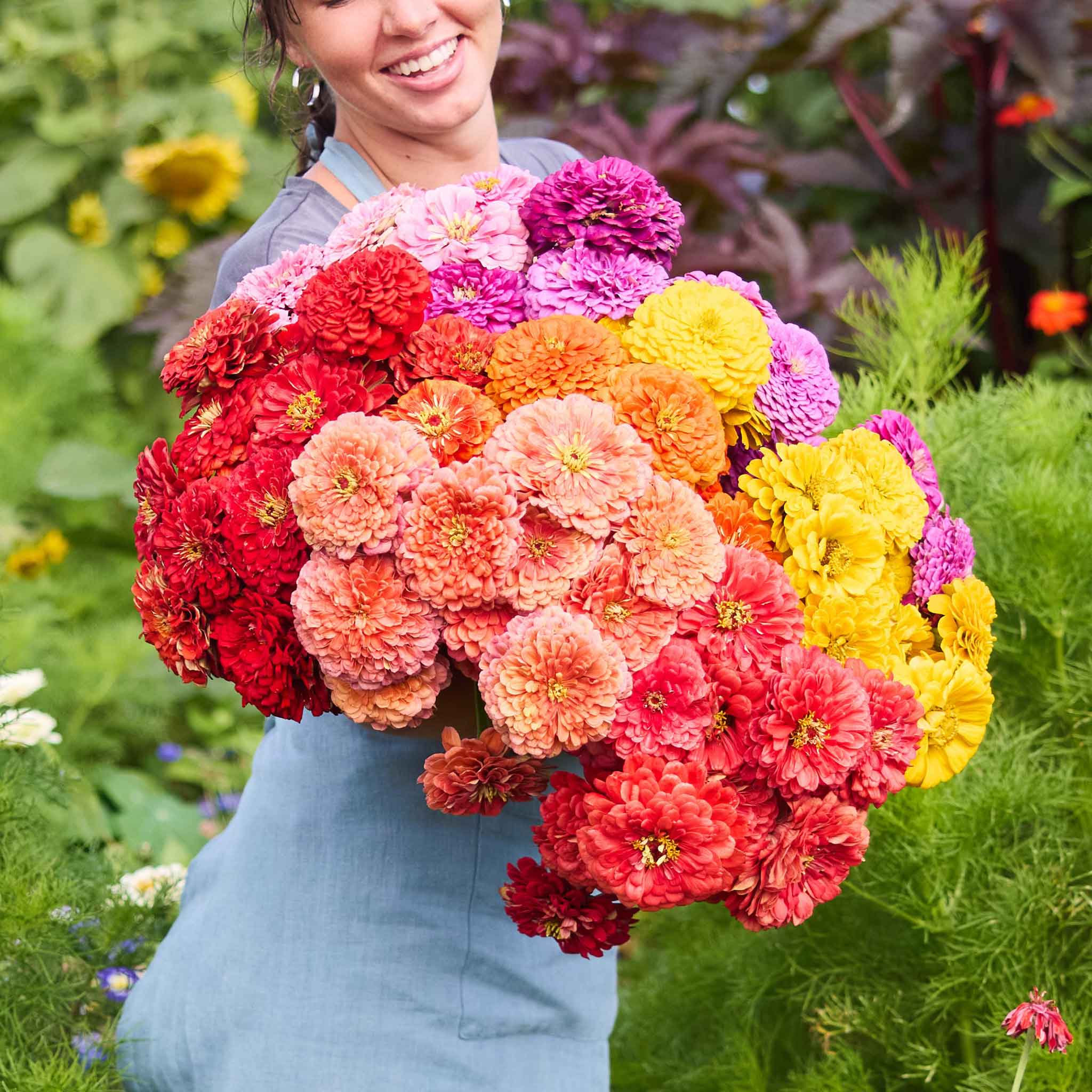 A woman holding a bouquet of benary giant mix zinnia flowers with green leaves in the background.