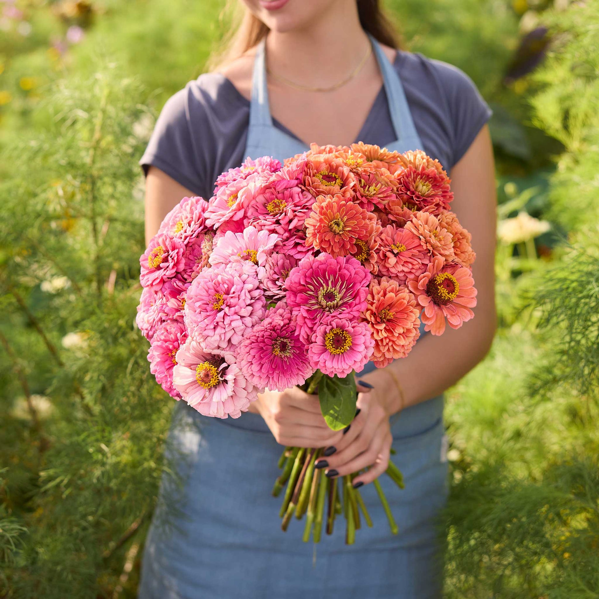 Person holding a bouquet of flowers from the zinnia benary pink coral bundle in a garden setting