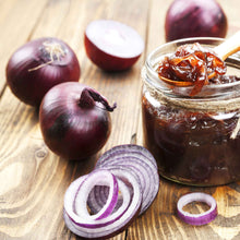 A close-up of several sliced Red Carpet onions with thin, papery skins, resting on a rustic wooden surface.