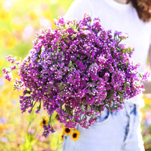 Statice twilight purple round bouquet held up with yellow flowers visible in the background