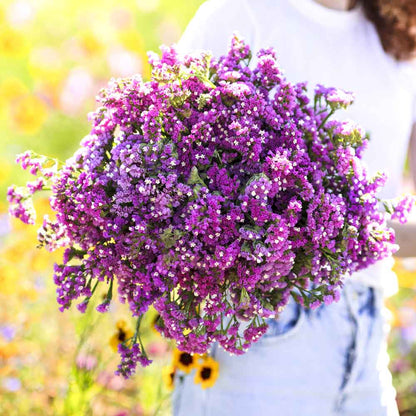 Statice twilight purple round bouquet held up with yellow flowers visible in the background