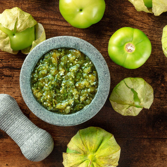 Green tomatillo fruit with a bowl of salsa made with tomatillo.