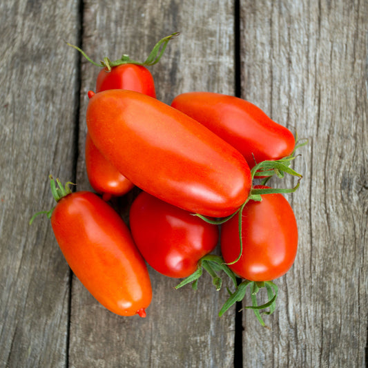 A cluster of ripe red Roma tomatoes shown on a wooden background.
