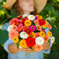 Person holding a bouquet of colorful pumila mix zinnia flowers in a garden setting